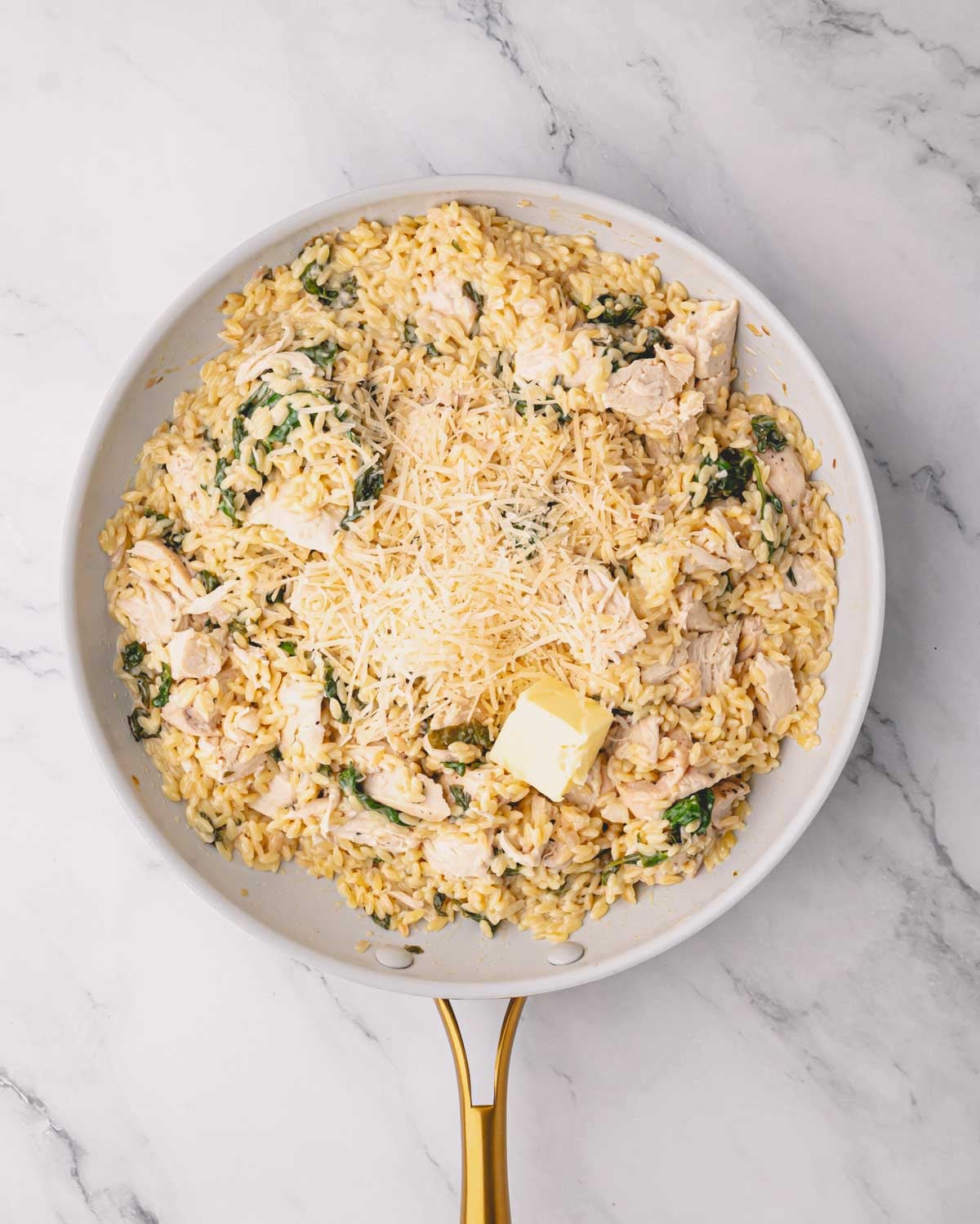 A white skillet with lemon chicken orzo cooking with parmesan and butter on top.