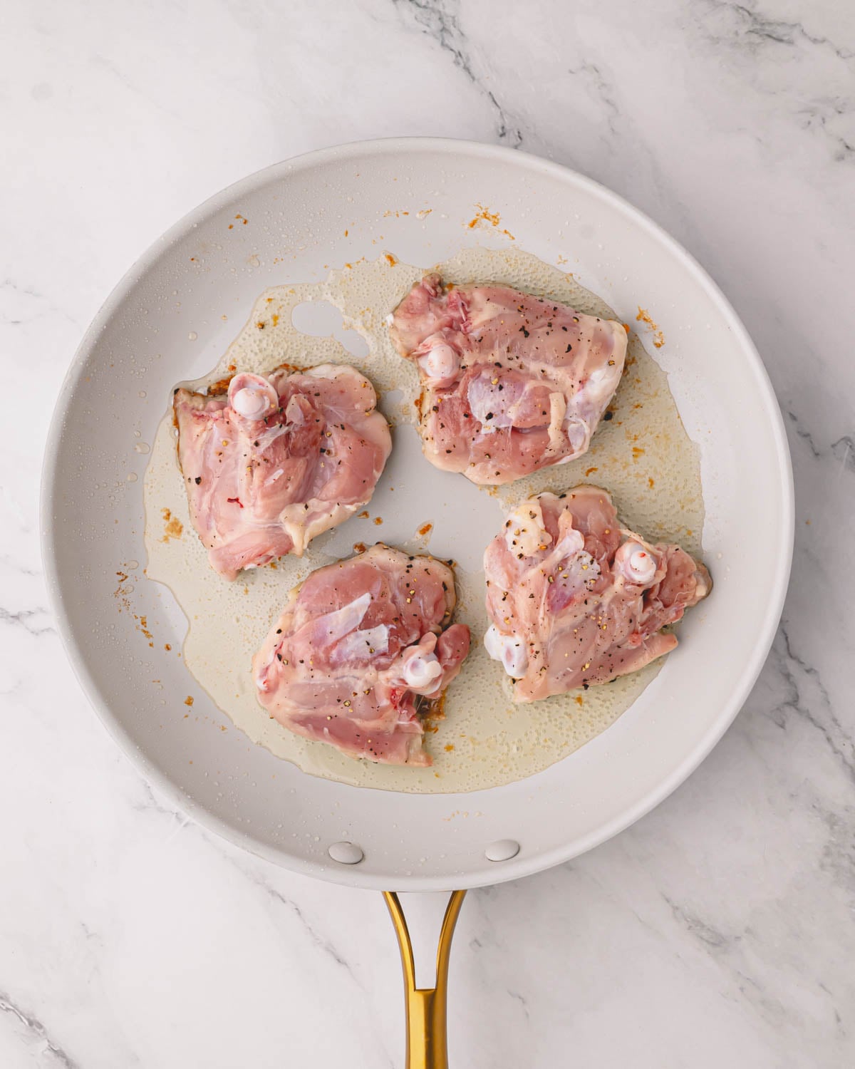 A white skillet with chicken thighs cooking skin-side down.