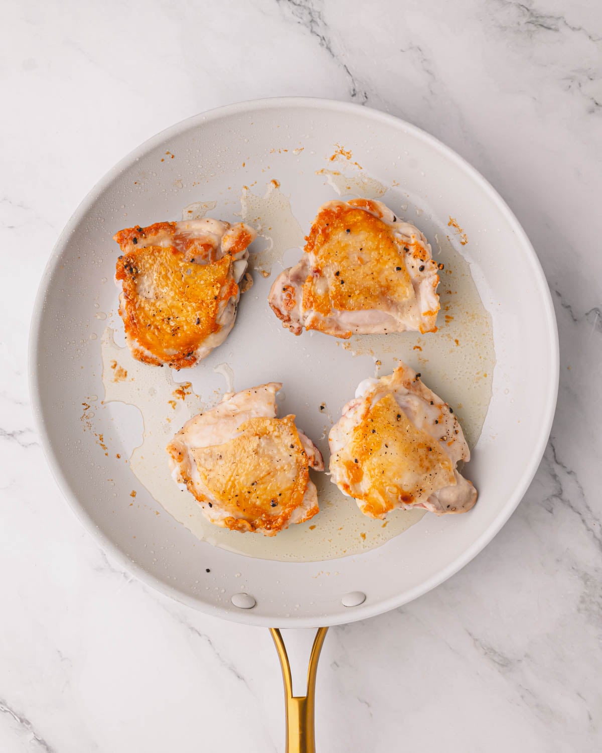 A white skillet with seared chicken thighs.