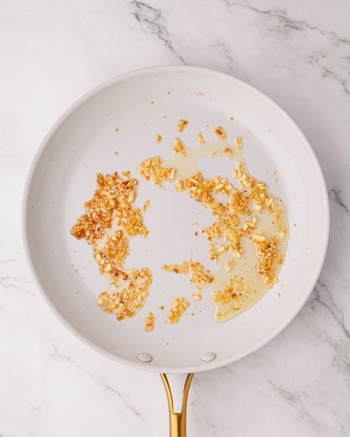 A white skillet cooking garlic and ginger.