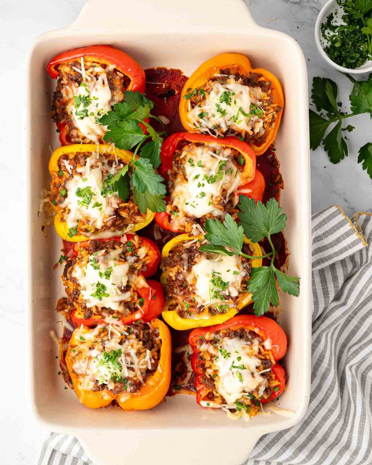 A white baking dish with stuffed peppers with ground beef and rice and parsley on top.