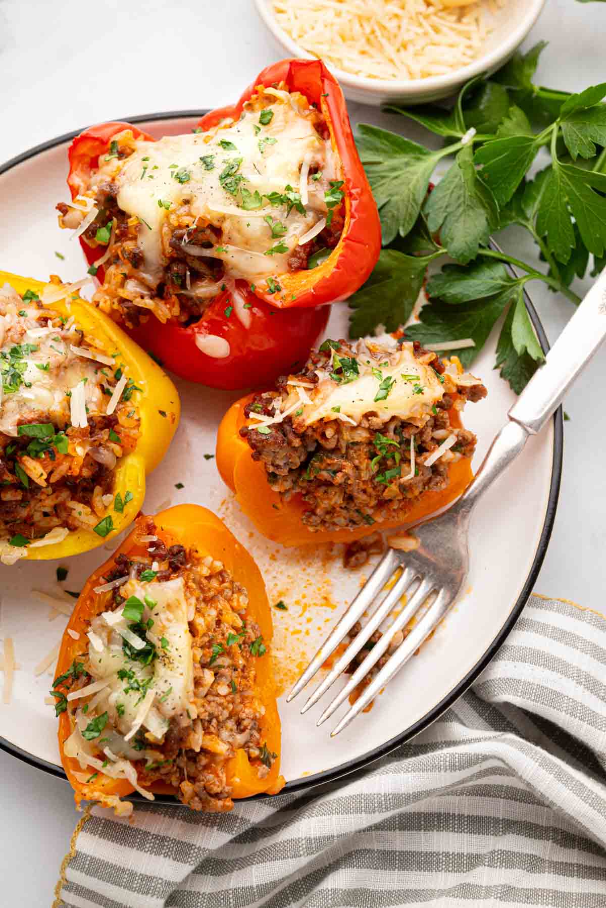 A white plate with stuffed bell peppers with ground beef and rice with a fork. One bell pepper is cut open.