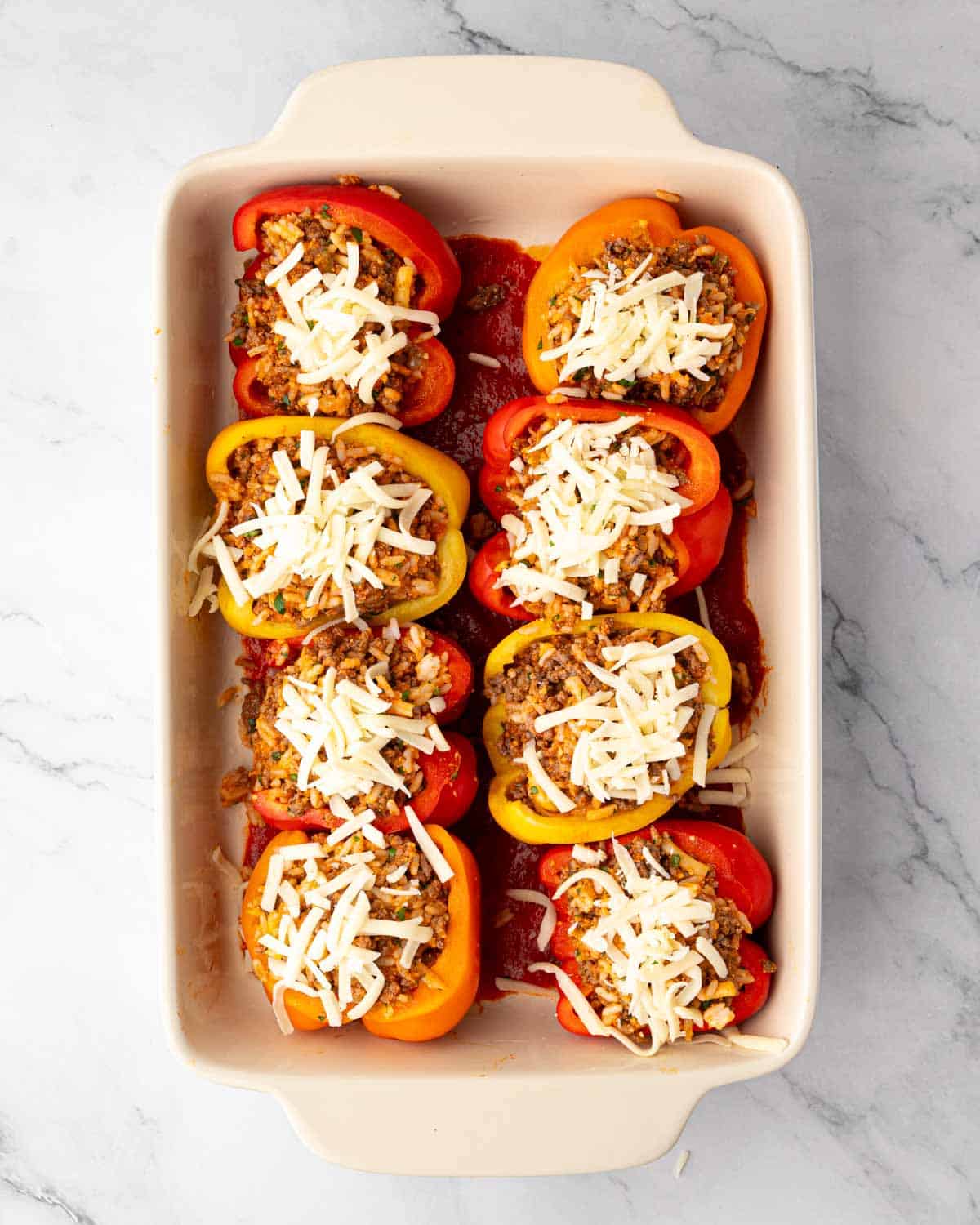 A white baking dish with stuffed bell pepper halves with shredded mozzarella cheese on top.