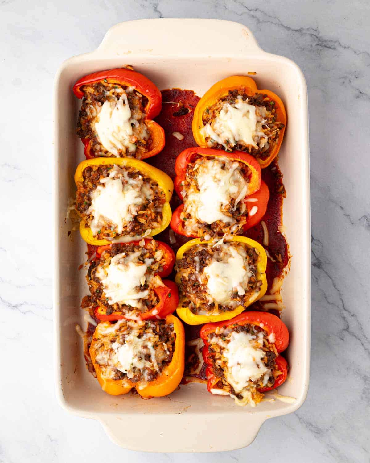Stuffed bell peppers with ground beef and rice baked in a white baking dish.