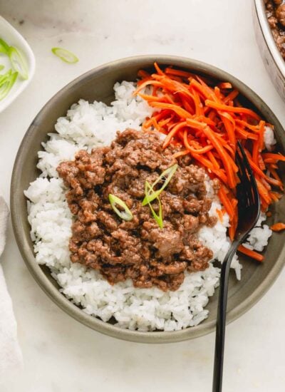 Teriyaki ground beef over rice with pickled carrots in a green bowl with a black fork.