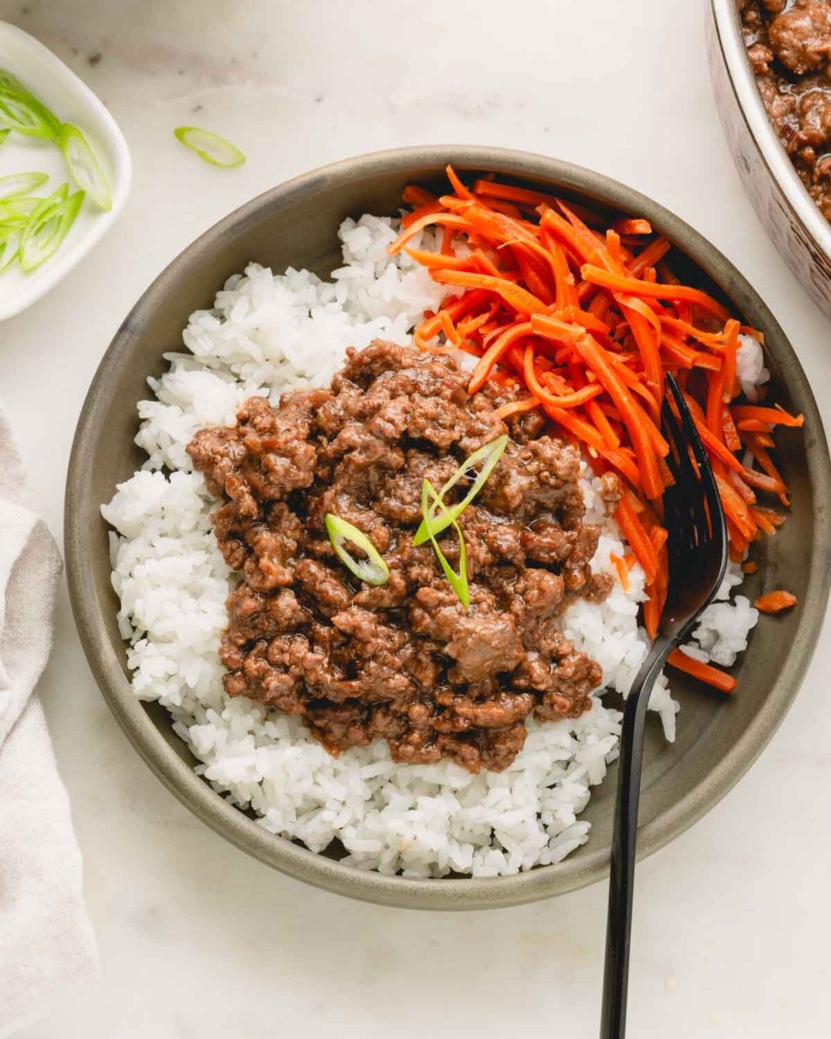 Teriyaki ground beef over rice with pickled carrots in a green bowl with a black fork.