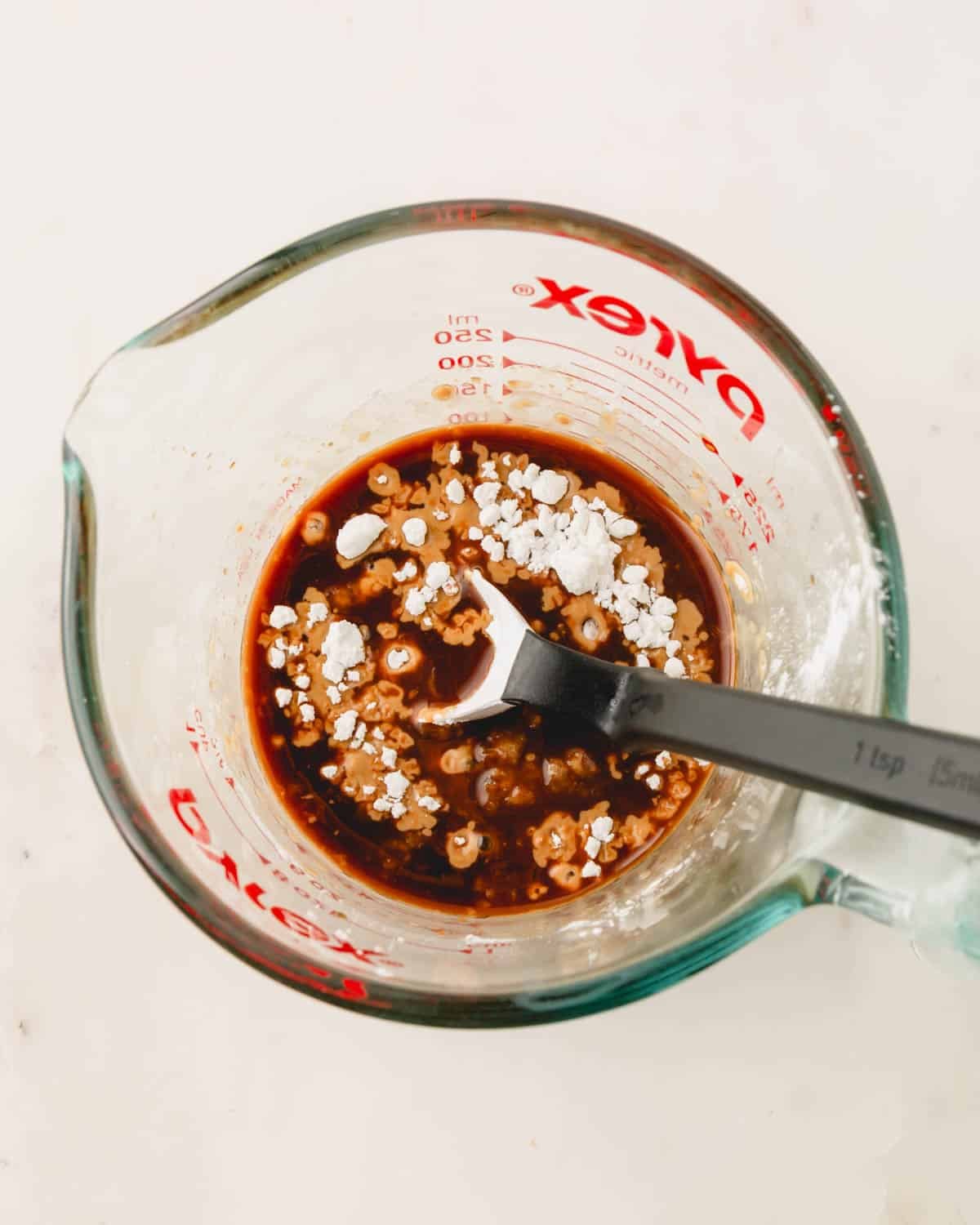 A measuring cup with ingredients for homemade teriyaki sauce and a measuring spoon.