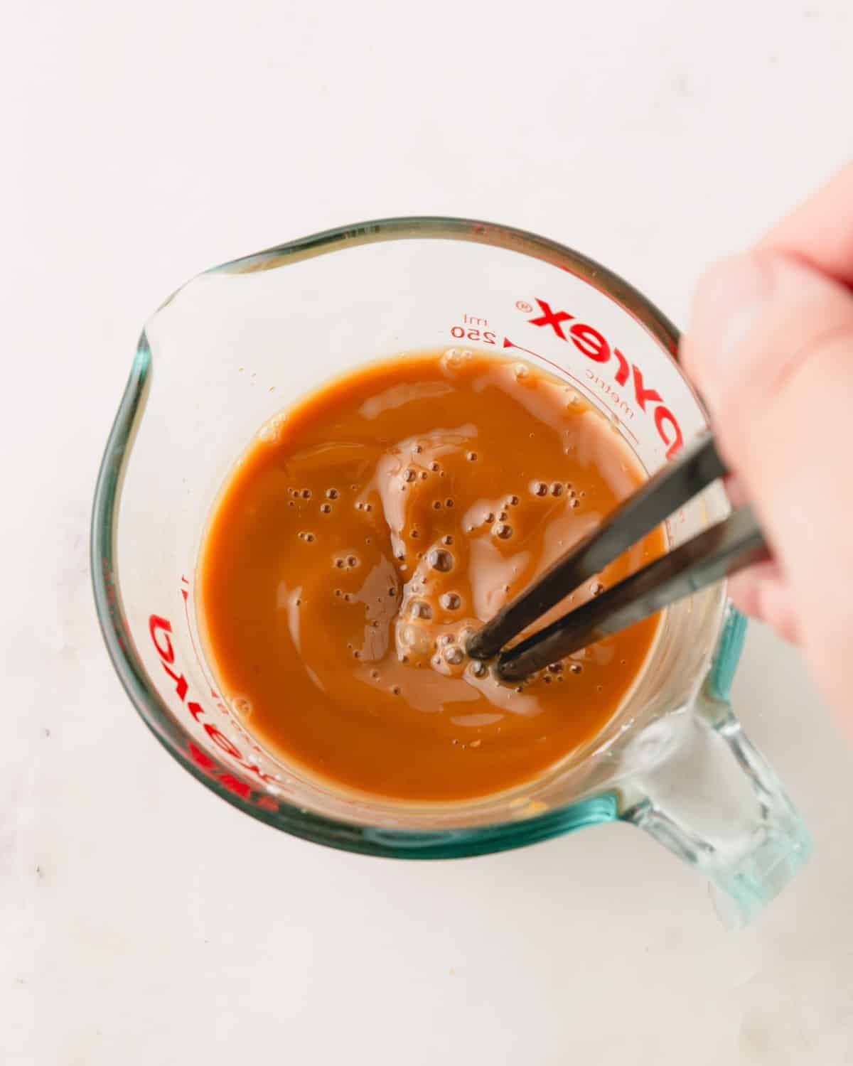 A hand using chopsticks to mix together the homemade teriyaki sauce in a glass measuring cup.