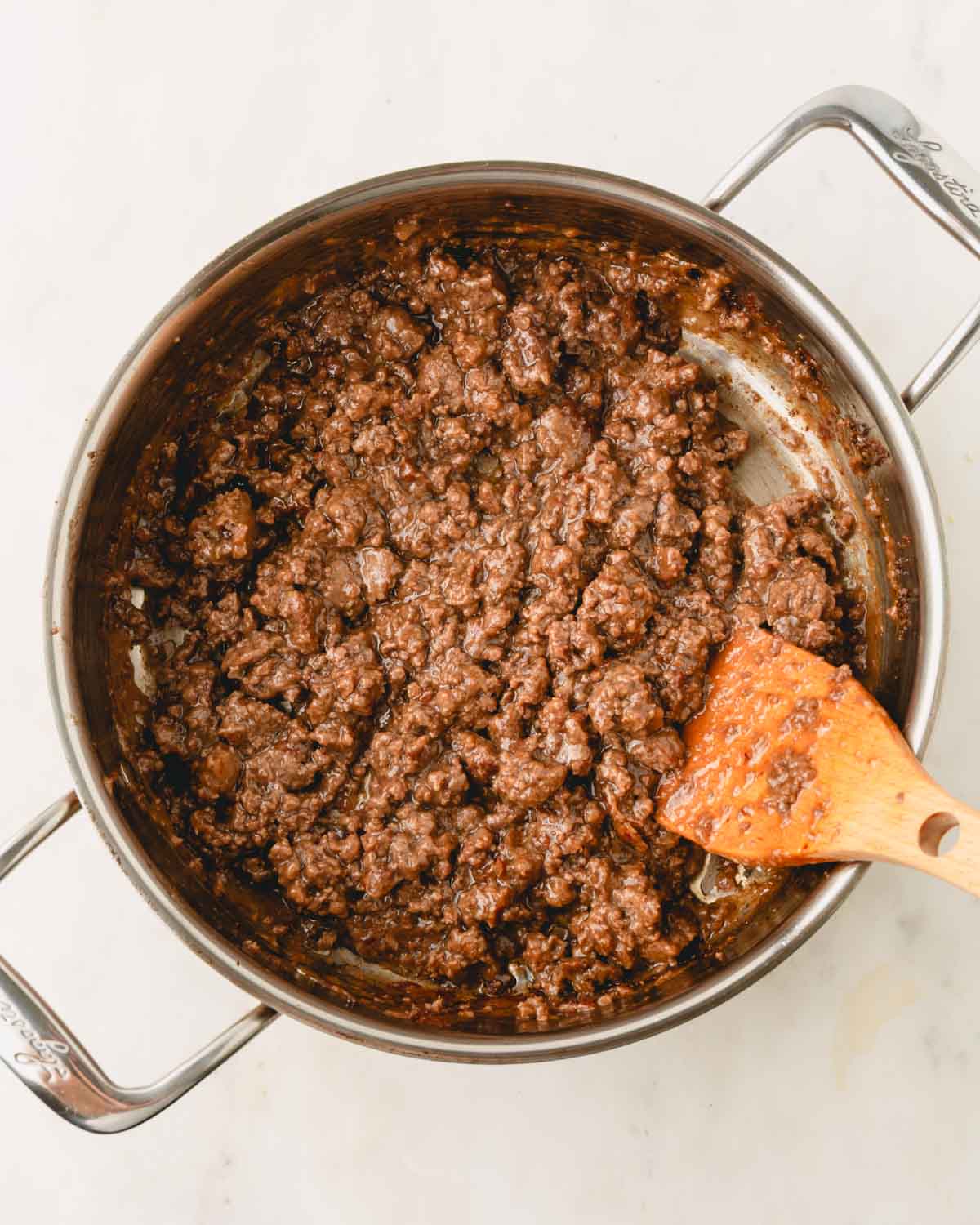 Ground beef teriyaki in a stainless steel skillet with a wooden spoon.