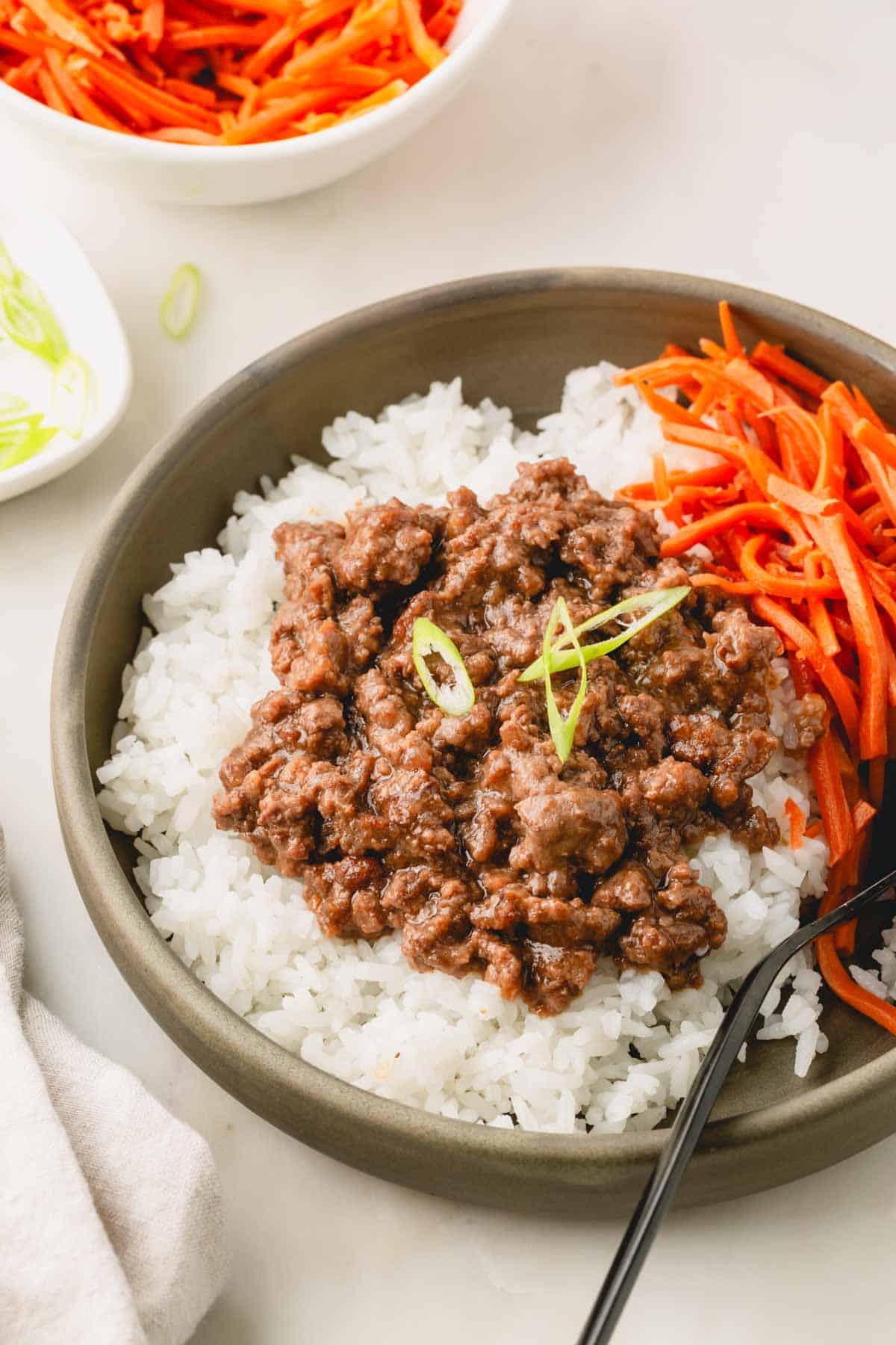 Teriyaki ground over white rice with pickled carrots in a green bowl.