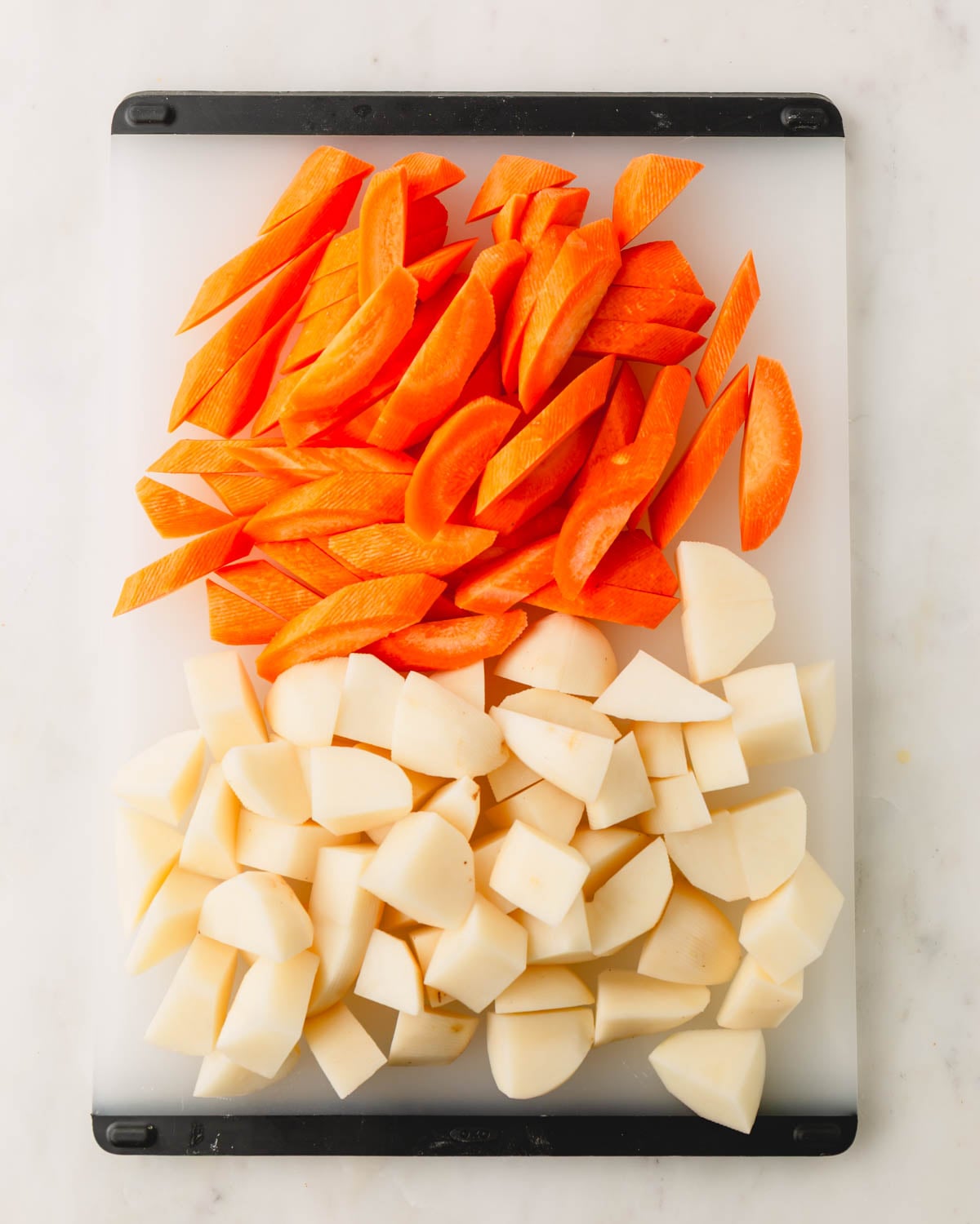 A plastic cutting board with cut carrots and potatoes.