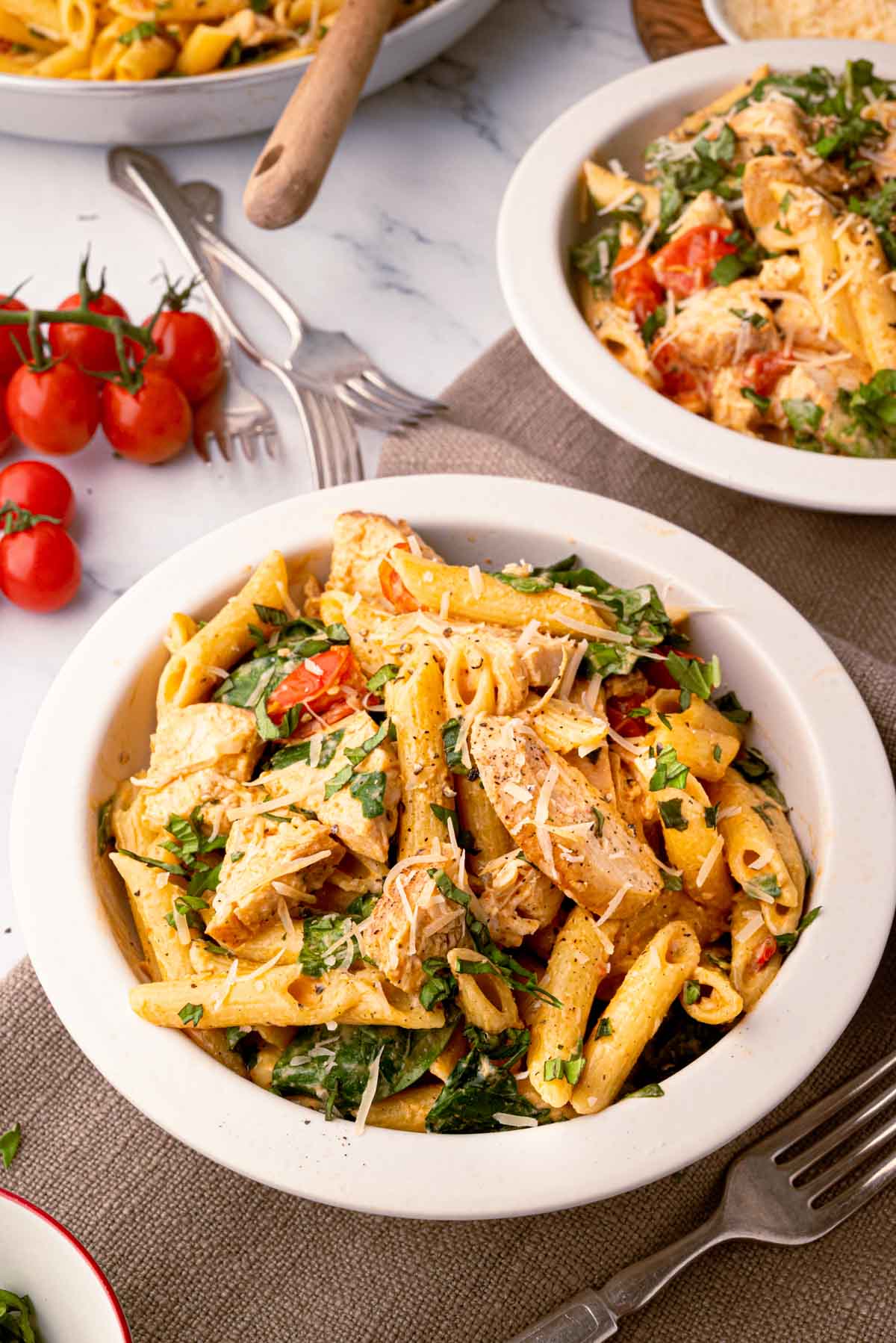 Two white bowls of boursin chicken pasta on a brown linen.