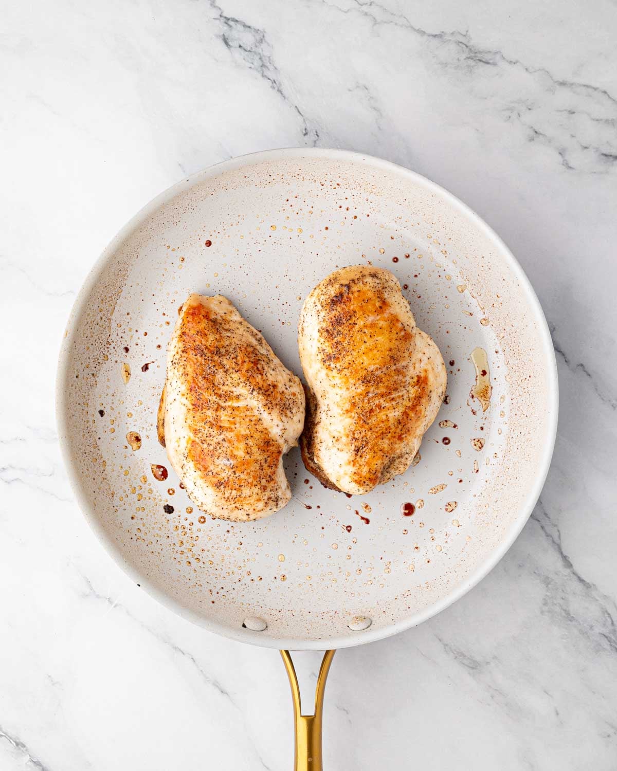 A white skillet with cooked boneless, skinless chicken breasts.