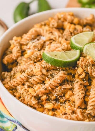 Close up image of elote pasta salad in a white bowl with lime wedges on top.