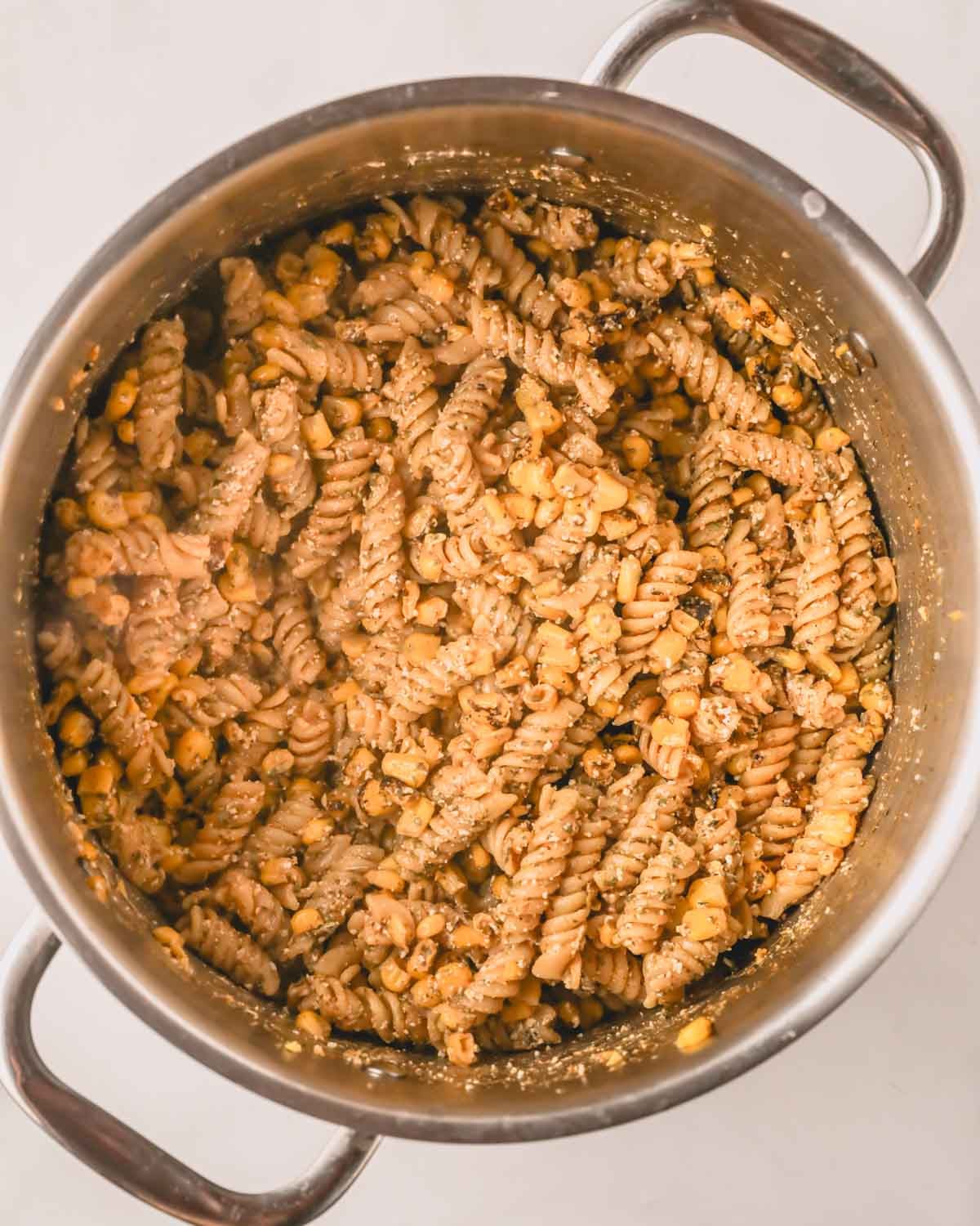 A stainless pot with pasta, corn, and cotija cheese stirred in a creamy dressing.