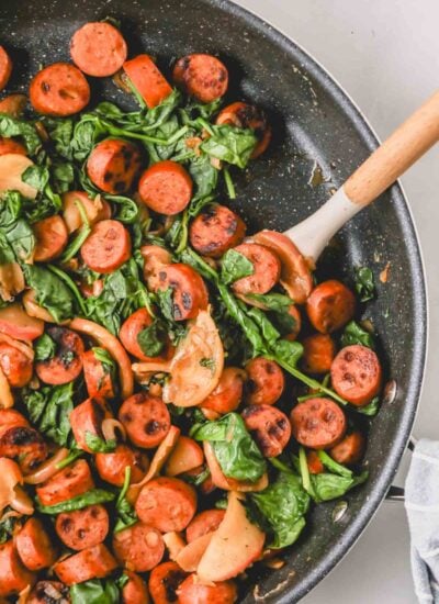 Chicken sausage and apples in a dark skillet with a wooden spatula.