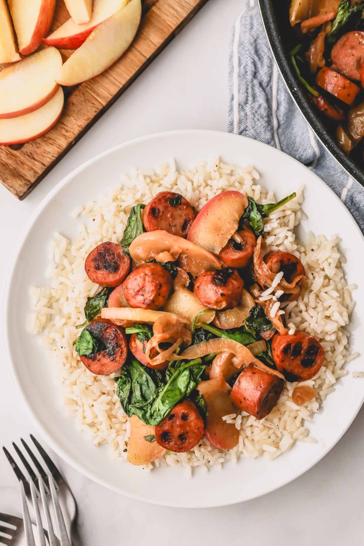 A white plate with rice and chicken sausage and apples on top.