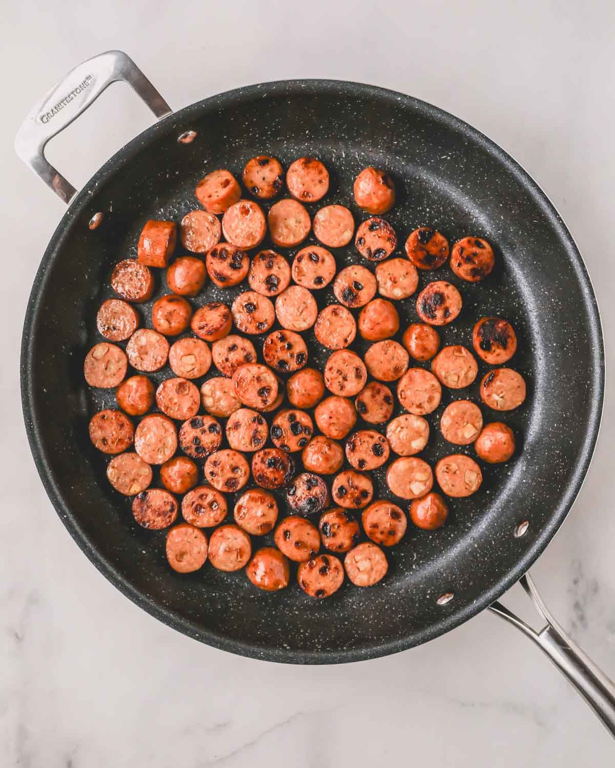 A large black skillet with seared chicken sausage.