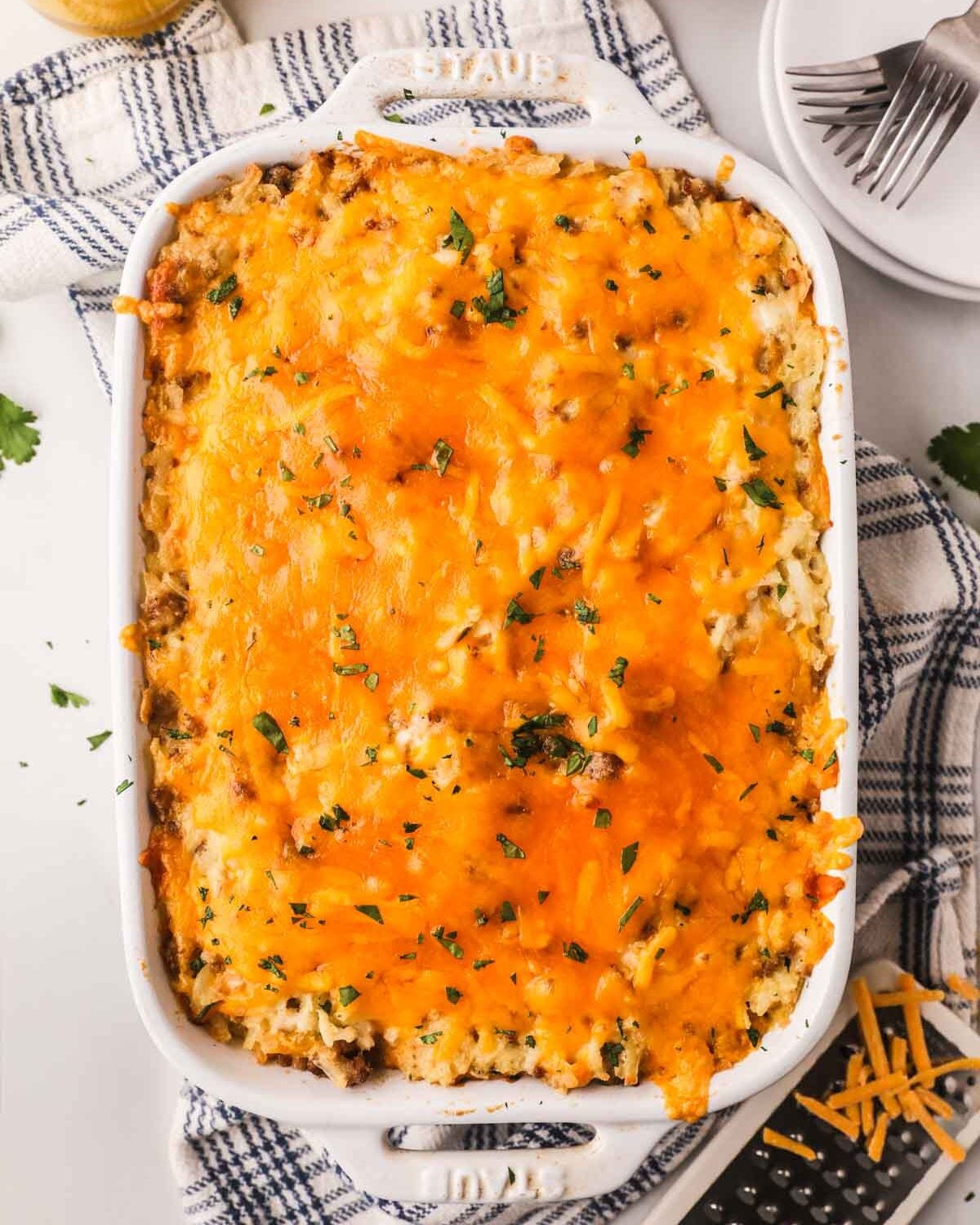 Baked sausage and hash brown casserole in a white baking dish with a plaid linen underneath.