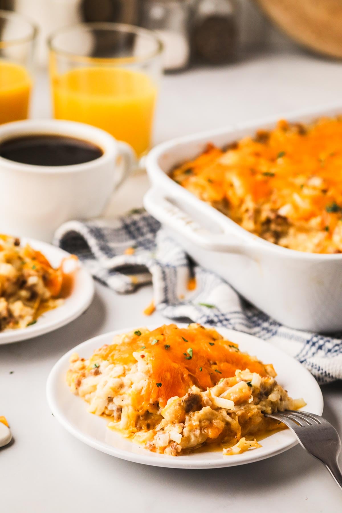 A small white plate of sausage and hash brown casserole with a larger white baking dish in the back.