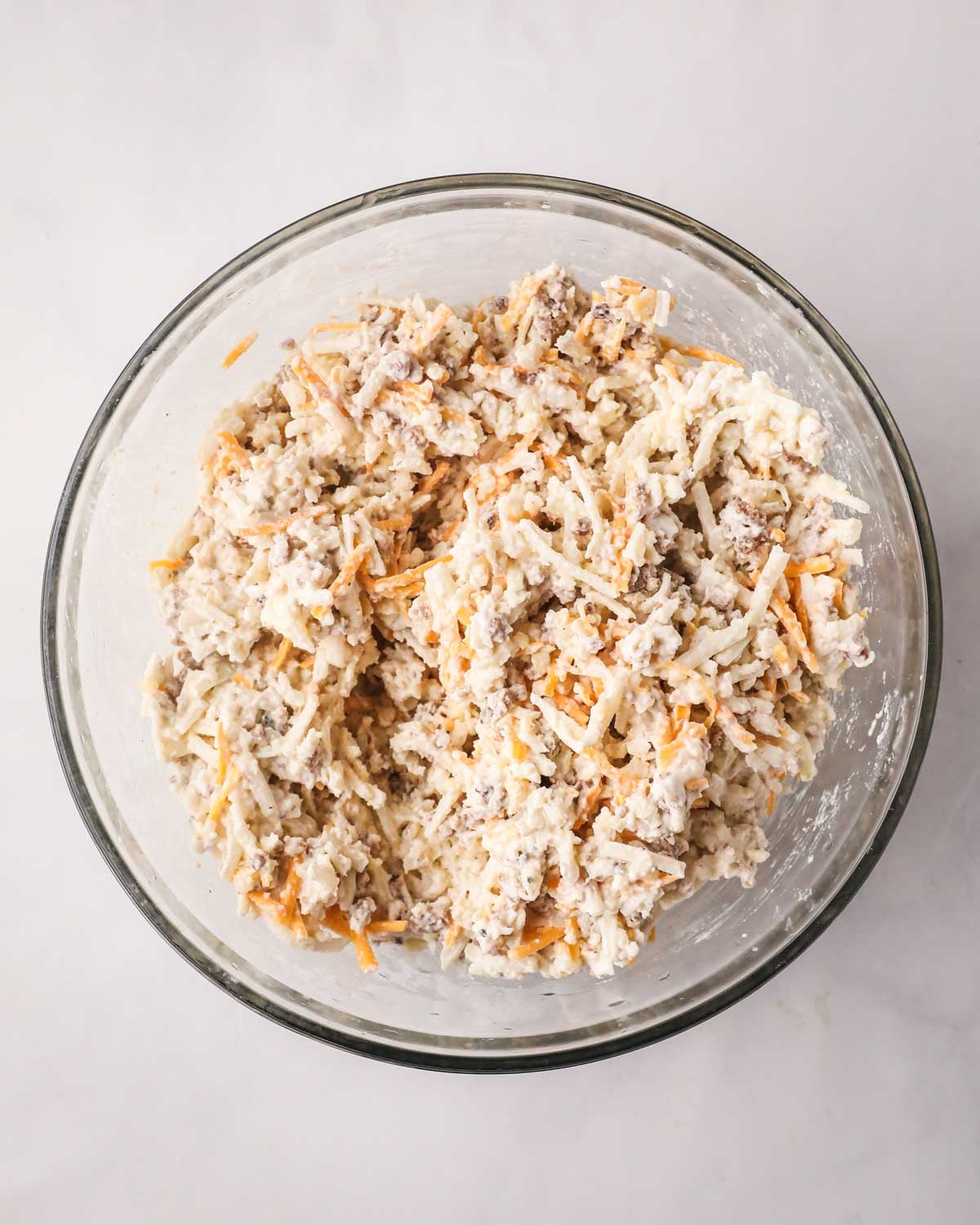 A glass bowl with hash brown and cheese mixture.