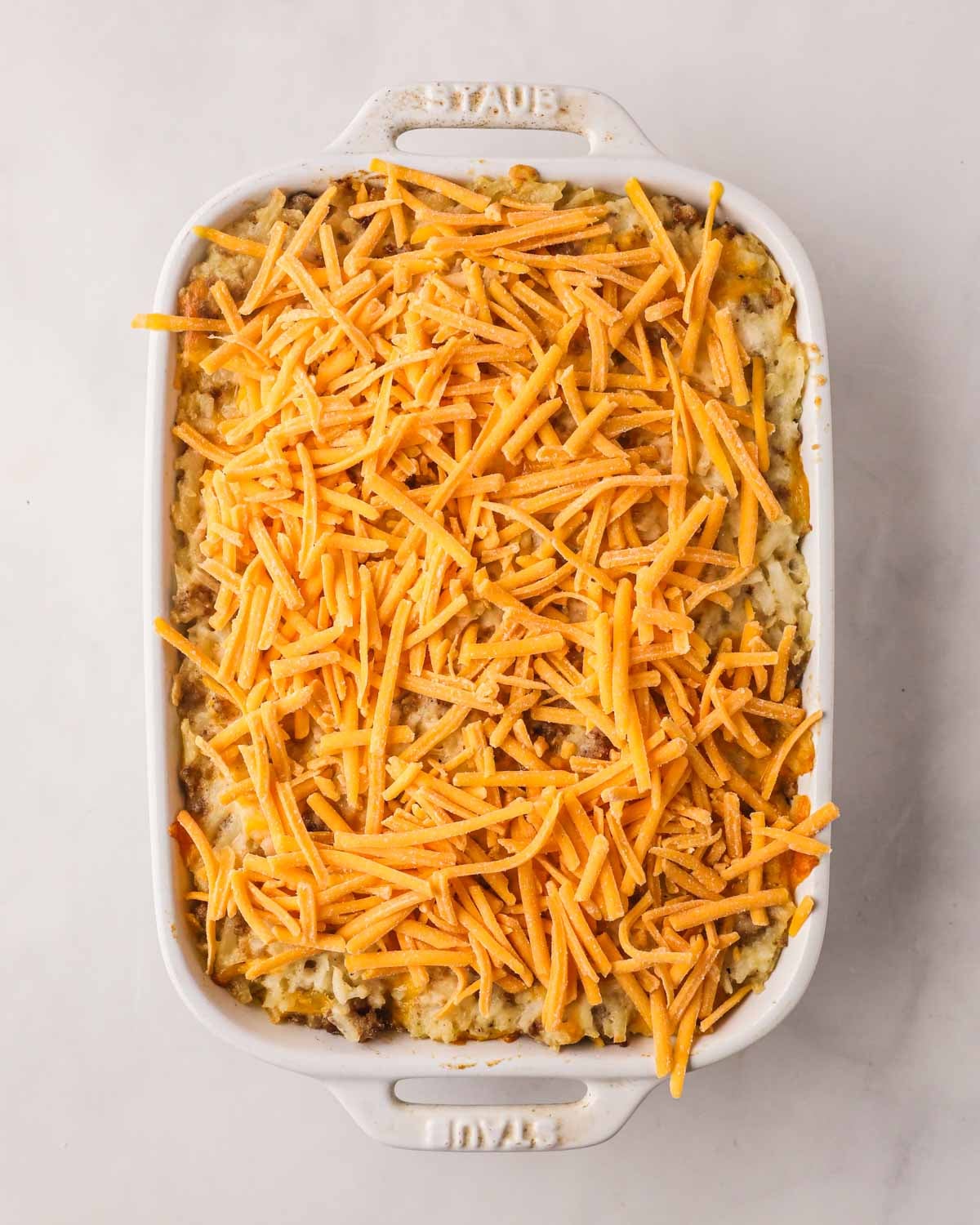 More shredded cheese on top of cheesy sausage hash brown casserole.