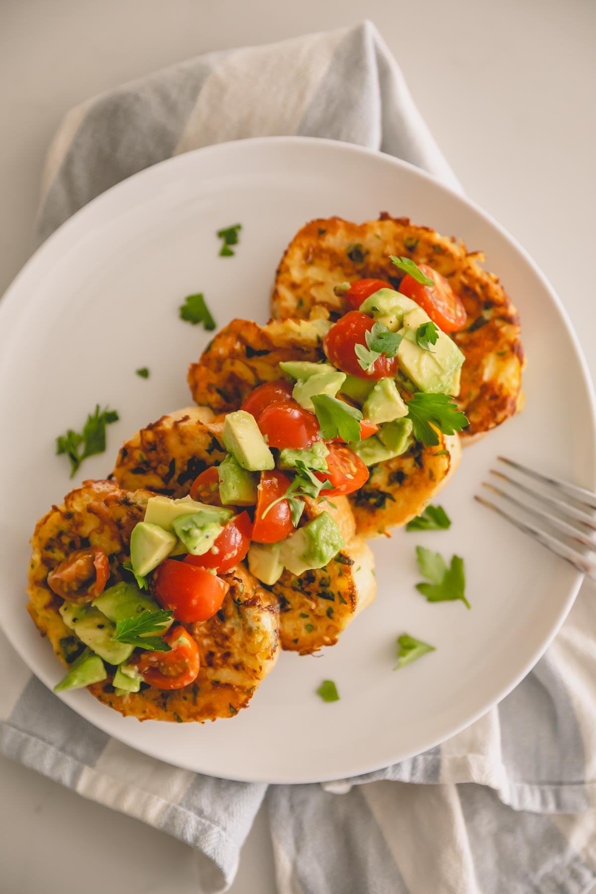 A white plate with savory french toast and avocado and cherry tomatoes on top. A fork is resting on the side.