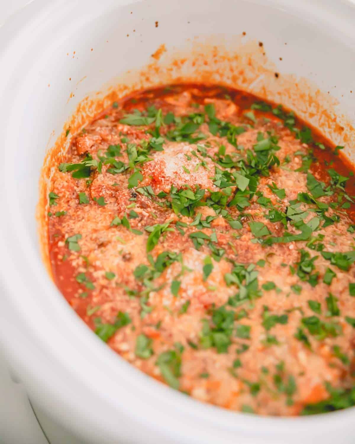 Slow cooker chicken cacciatore with parmesan cheese and parsley on top.