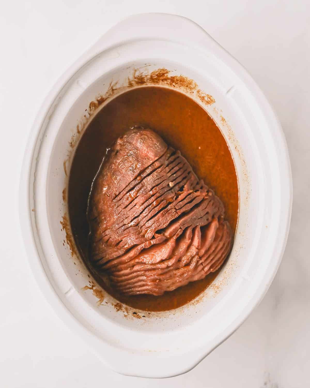 A white crock pot bowl with a cooked ham and honey glazed.
