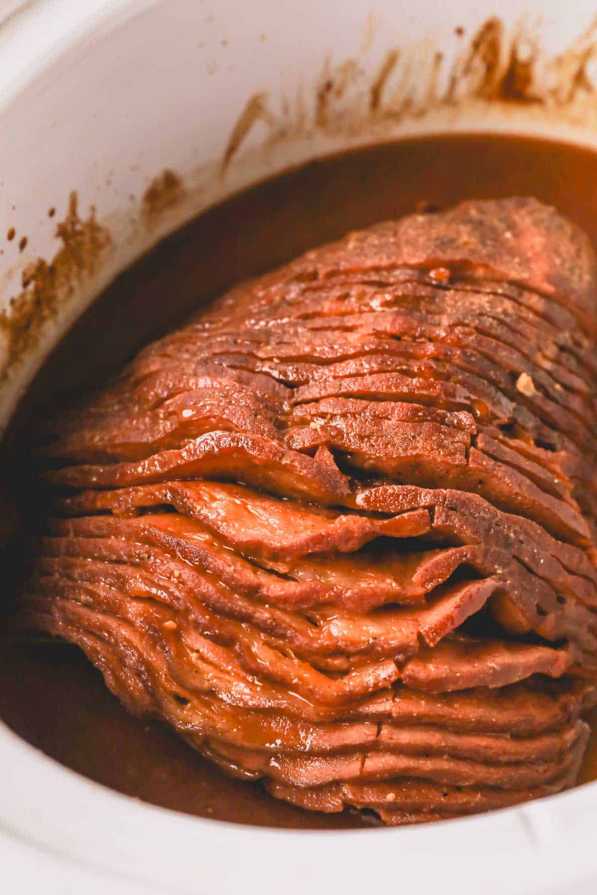 Close up image of slow cooker ham with honey glaze in white slow cooker bowl.