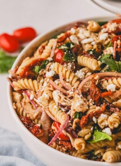 A close up image of sun dried tomato pasta salad in a white bowl.