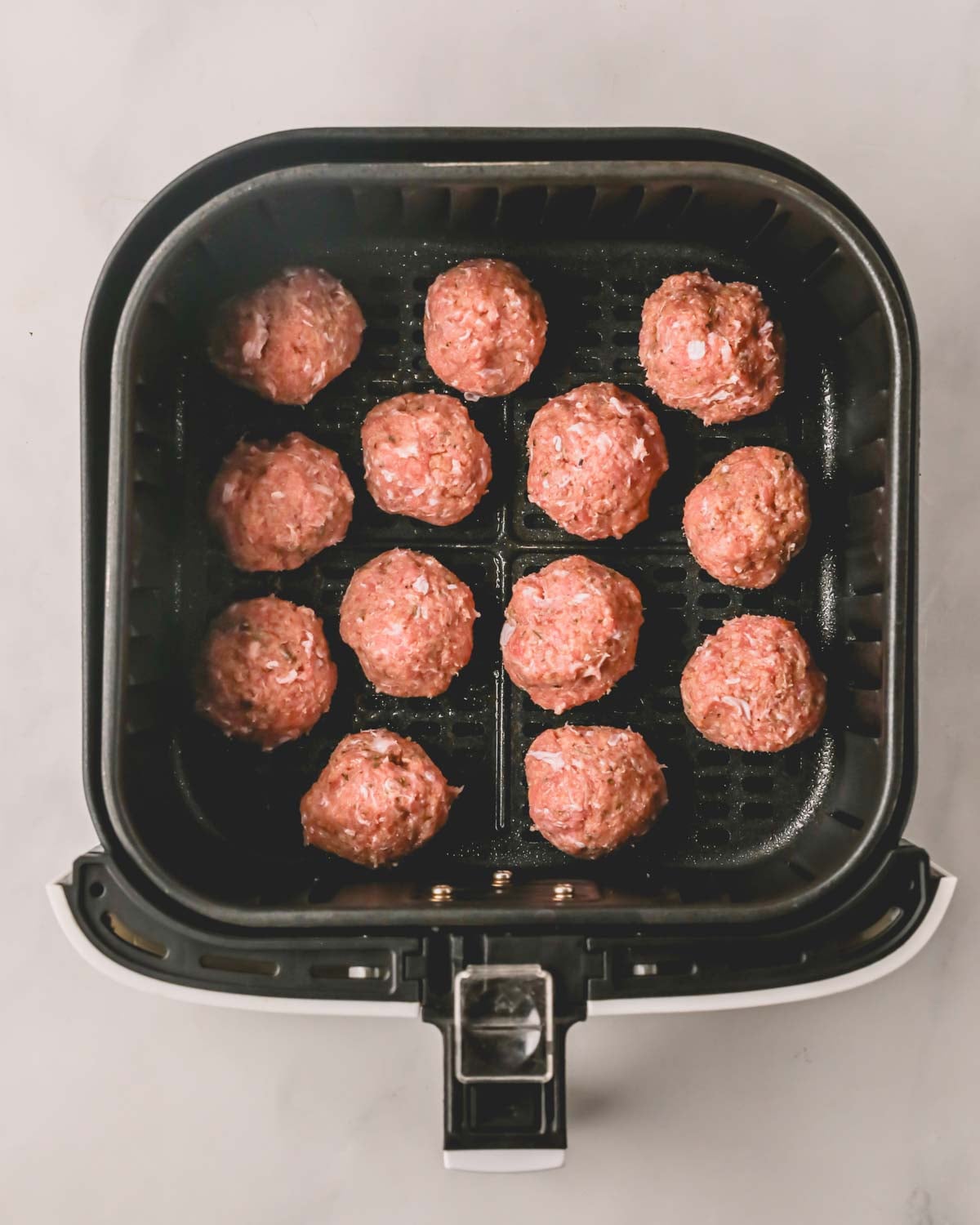 An air fryer bowl with shaped turkey meatballs before cooking.