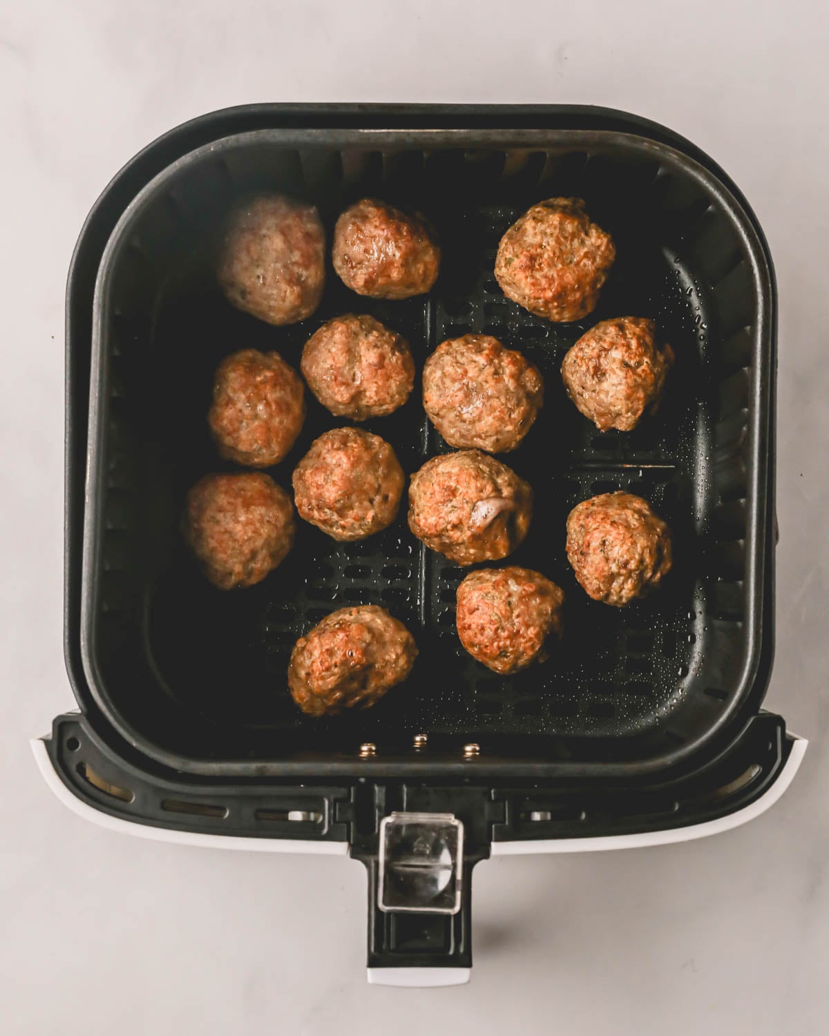An air fryer with cooked turkey meatballs.