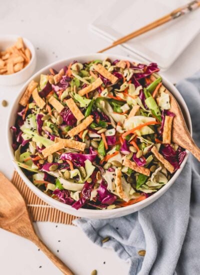 Crunchy Asian slaw in a white bowl with wooden spoons.