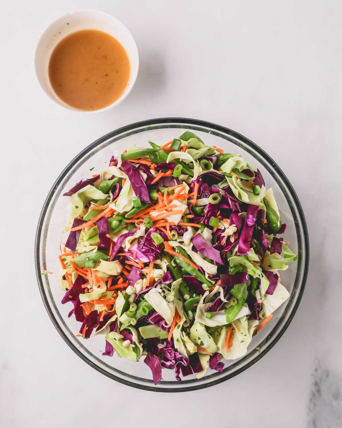 A glass bowl with crunch Asian slaw ingredients with dressing on the side.