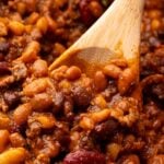 A wooden spoon scooping up cowboy baked beans.