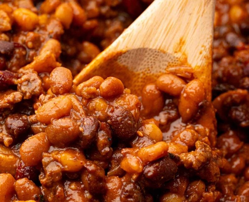 A wooden spoon scooping up cowboy baked beans.