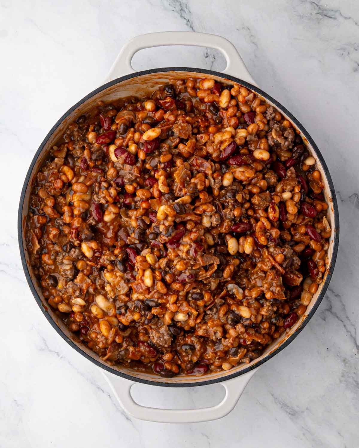 A white braiser with cowboy baked beans mixed ready to bake.