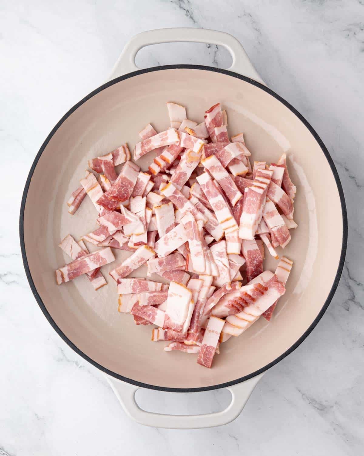 A white braiser with sliced bacon cooking.