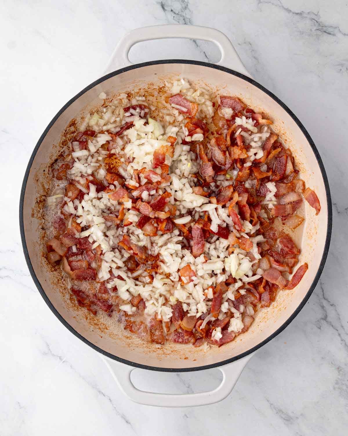 A white braiser with onion and bacon cooking.