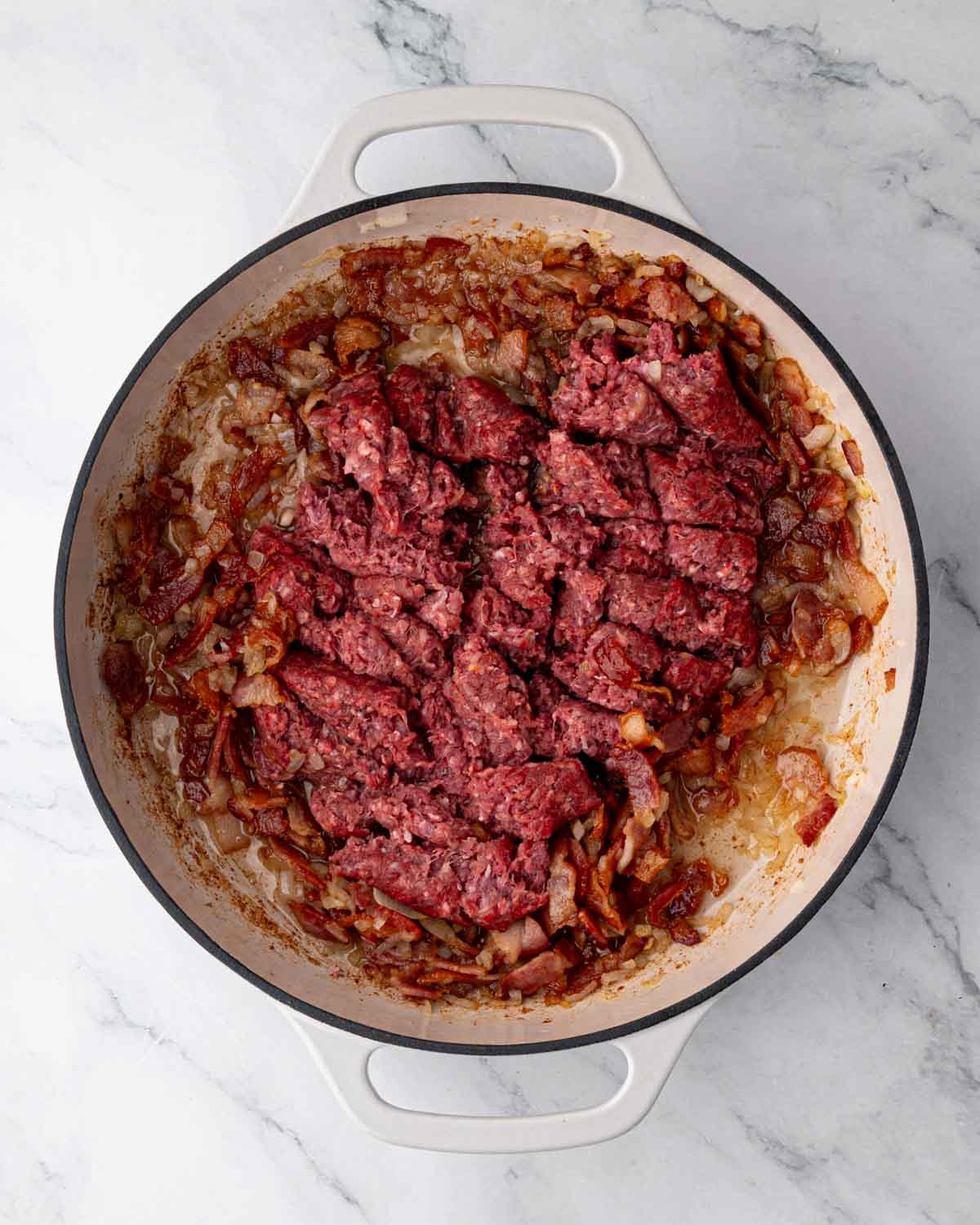 A white braiser with onion, bacon, and ground beef cooking.