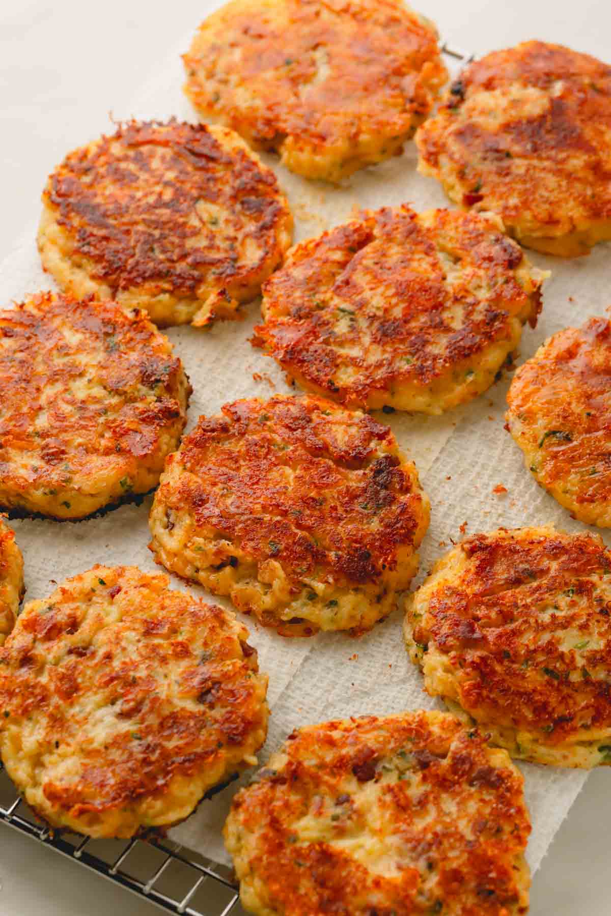 Fried mashed potato patties on a paper towel over a wire baking rack.