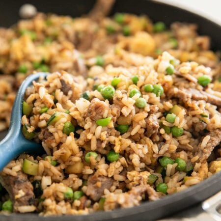 A skillet with steak fried rice and a blue spoon.