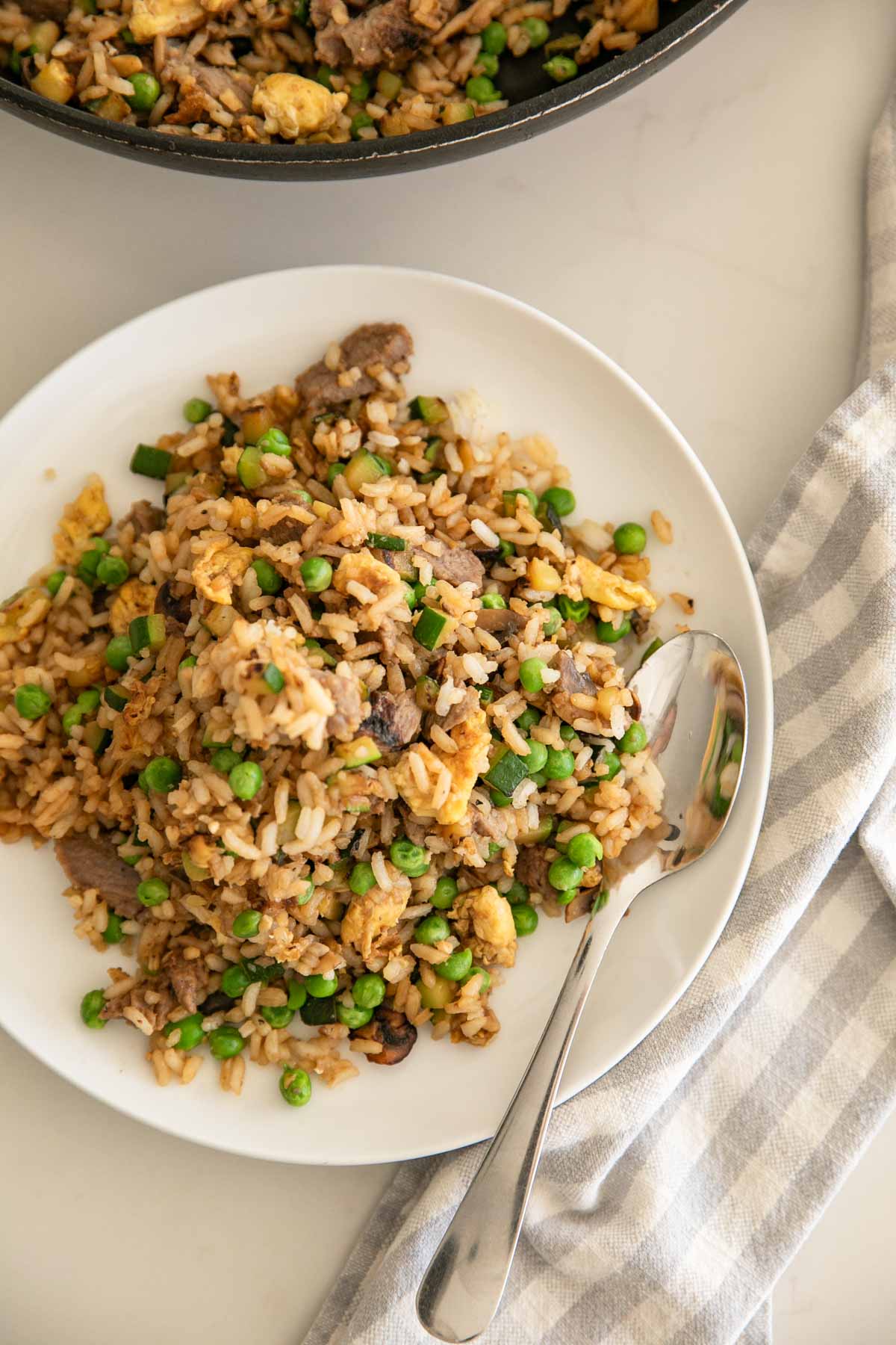 A white plate with steak fried rice and a spoon on the side.