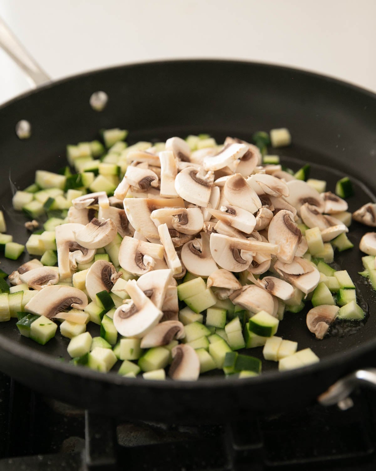 A skillet with mushrooms and zucchini cooking.