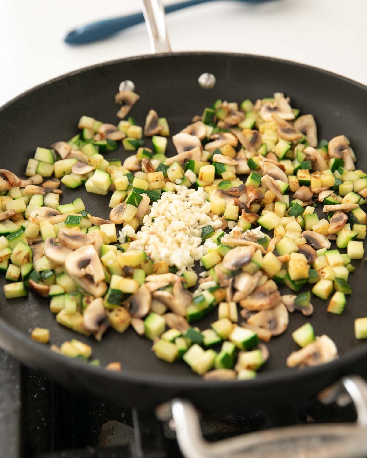 A skillet with zucchini, mushrooms, and garlic cooking.
