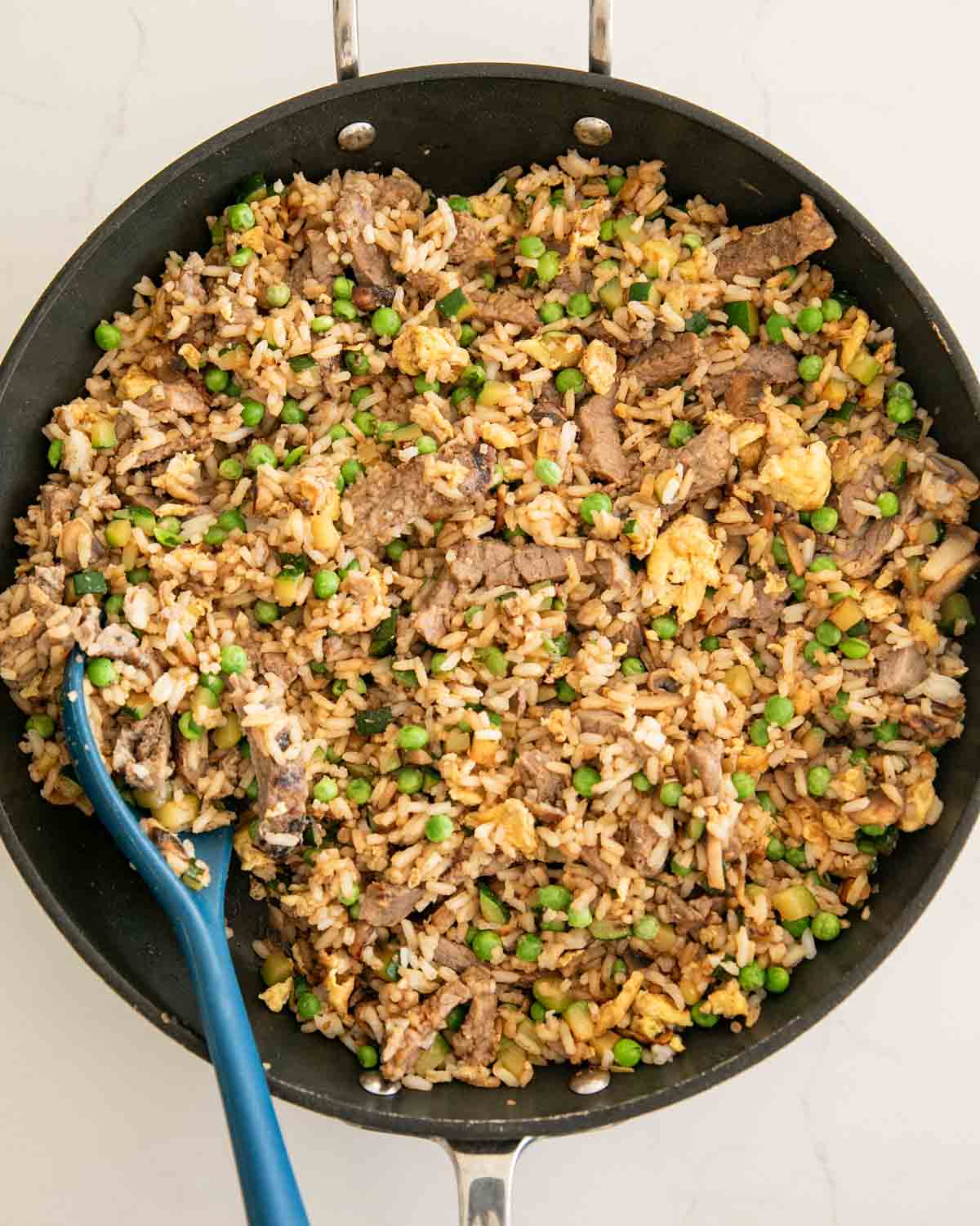 A skillet with steak fried rice and a blue spoon.