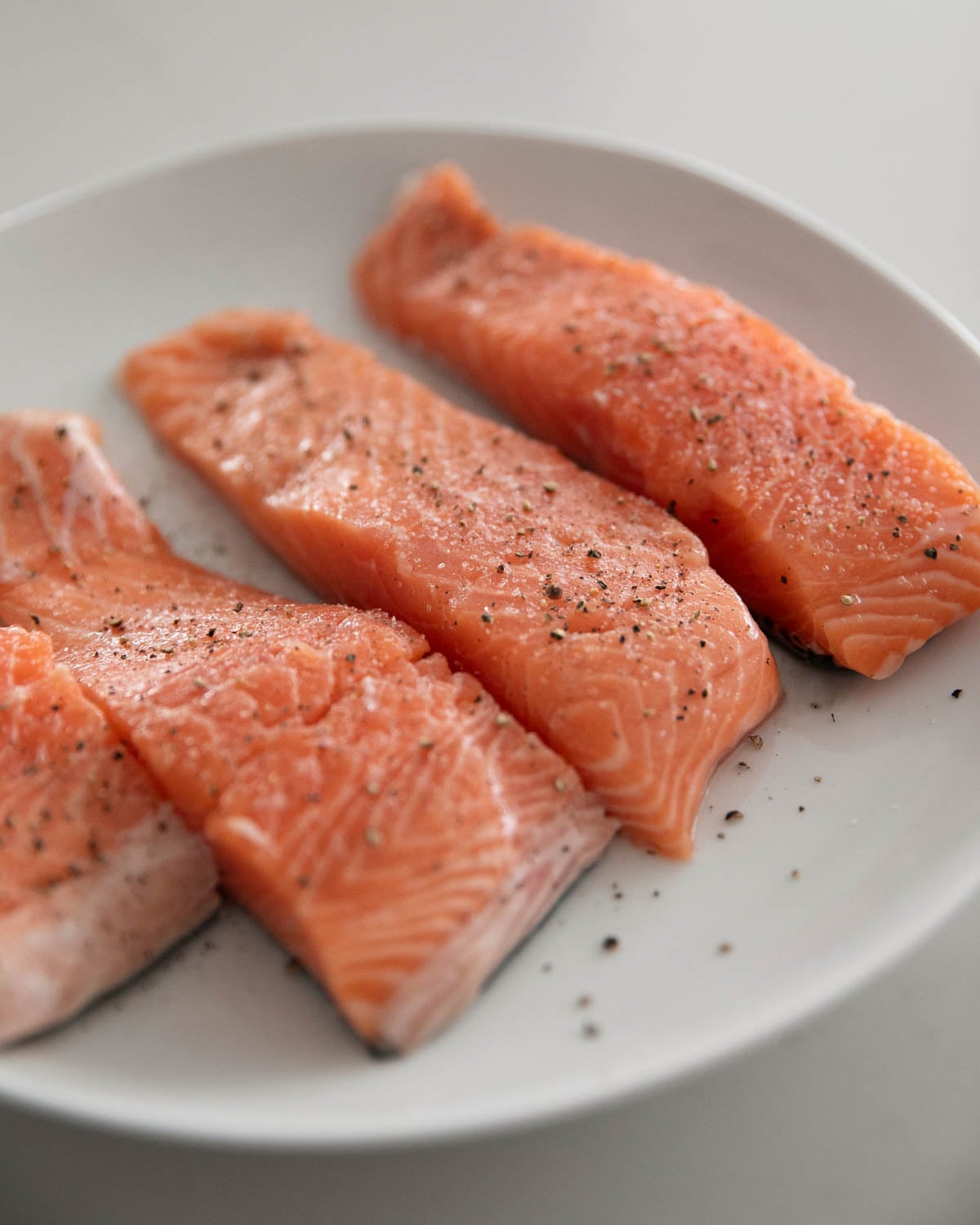 Steelhead trout fillets seasoned with salt and pepper on a white plate.