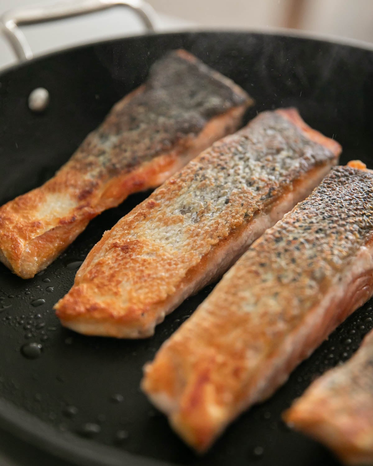 Steelhead trout slices skin side up searing in a black skillet.