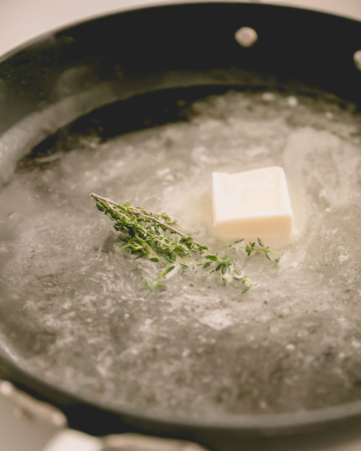 A black skillet with butter melting and thyme sprigs.